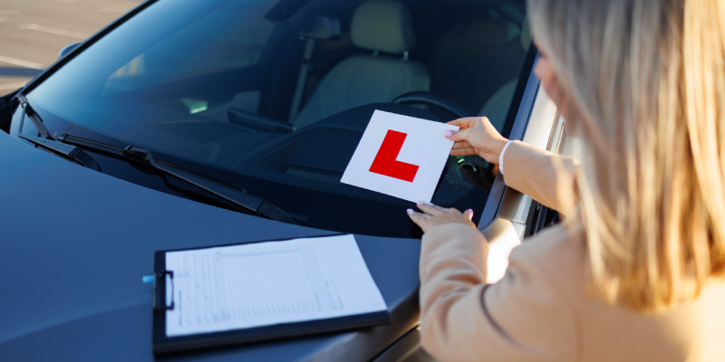 Woman placing l-plate onto car windscreen