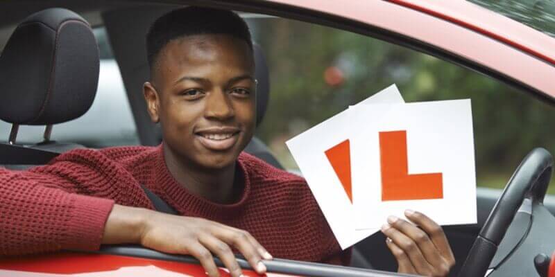 Boy in drivers seat holding learner signs up
