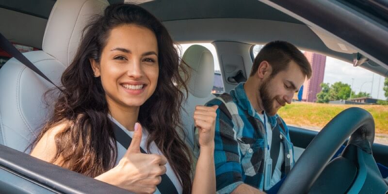 Girl smiling with thumbs up next to driving instructor inside car